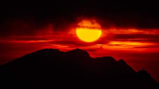 Sonnenuntergang hinter einer Bergsilhouette mit leuchtend roten und orangefarbenen Wolken am Himmel.