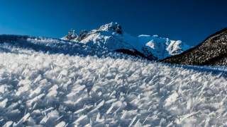 Schneebedecktes Feld mit spitzen Eiskristallen vor schneebedeckten Bergen unter klarem blauen Himmel.