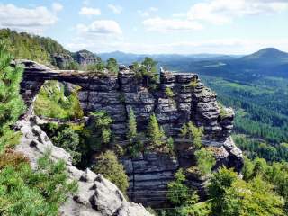 Natürliche Felsformation mit einer Felsbrücke, umgeben von Wald und Bergen unter blauem Himmel.