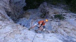 Zwei Personen klettern mit Helmen und Kletterausrüstung an einer steilen Felswand.