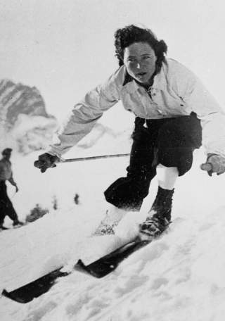 Schwarz-weiß Foto einer konzentrierten Person beim schnellen Skifahren auf einer schneebedeckten Piste, mit einem weiteren Skifahrer im Hintergrund.