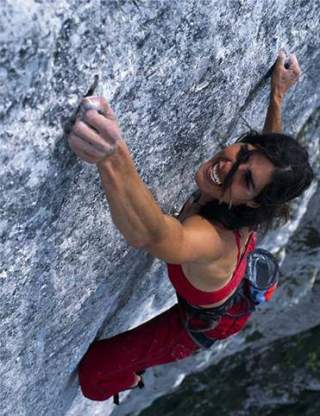 Eine Frau klettert an einer steilen Felswand, trägt rote Sportkleidung und zeigt einen kraftvollen Gesichtsausdruck.