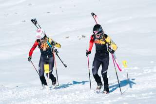 Zwei Skibergsteiger*innen laufen über eine verschneite Ebene.