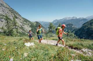 Wander*innen im Sommer im Aufstieg vor einem Bergpanorama