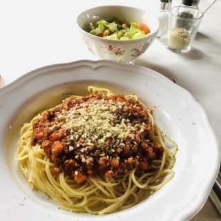 Teller mit Spaghetti Bolognese, garniert mit geriebenem Käse, im Hintergrund eine Schüssel mit gemischtem Gemüse.