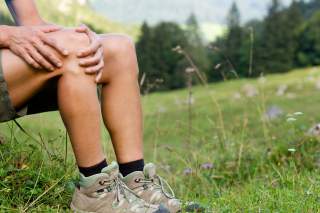 Mensch in Wanderschuhen hält sich das schmerzende Knie