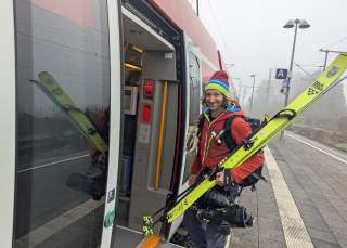 Bernhard Agerer steigt bepackt mit Skiern und Skischuhen in einen Regionalzug.