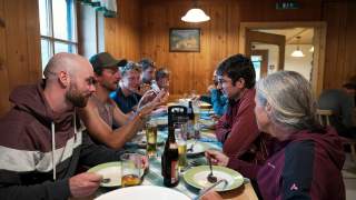 Gruppe sitzt beim Abendessen am Tisch in einer hölzernen Hüttenstube.