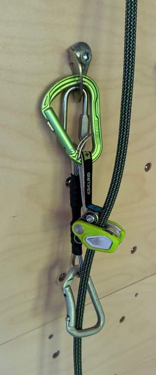 Kletterausrüstung mit Karabiner, Bremsassistent und Seil an einer Kletterwand befestigt.