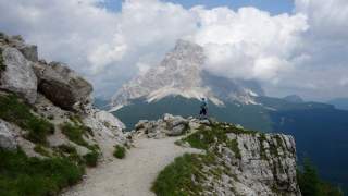 Wanderer steht auf felsigem Bergpfad und blickt auf einen wolkenverhangenen Berg in der Ferne.