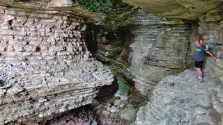 Zwei Männer stehen in einer engen, felsigen Schlucht mit sichtbaren Gesteinsschichten und einem kleinen Wasserlauf.