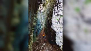 Drei Personen wandern durch eine schmale, felsige Schlucht mit hohen, zerklüfteten Wänden. Der Boden ist mit Steinen und Laub bedeckt.