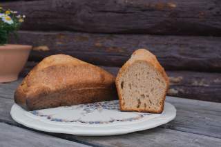 Ein Laib Sauerteigbrot und eine aufgeschnittene Brothälfte auf einem verzierten Teller, draußen auf einem Holztisch.