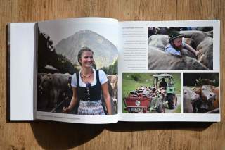 Aufgeschlagenes Buch mit Fotos vom Viehscheid: Links eine Frau in Tracht vor Kühen und Bergen, rechts oben ein Mann zwischen Kühen, darunter ein Traktor mit Milchkannen und zwei Kühe, eine davon mit Blumen geschmückt.