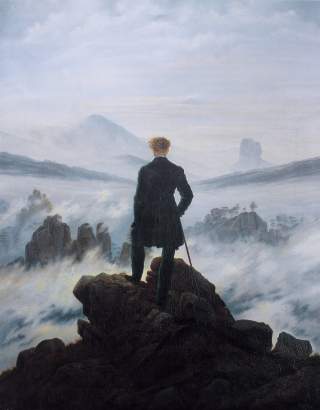 Eine Person steht auf einem Felsen und blickt in eine neblige Berglandschaft.