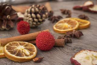 Getrocknete Orangenscheiben, Zimtstangen, rote dekorative Kugeln und Tannenzapfen liegen auf einer Holzoberfläche.