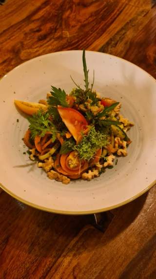 Teller mit frisch zubereitetem Salat aus Tomaten, Gurken, Blattsalaten, Kräutern und Walnüssen auf hölzernem Tisch.