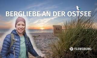 Frau in Outdoor-Bekleidung vor einem Ostseestrand mit Gras und Sonnenuntergang, Text „Bergliebe an der Ostsee“ und Logo „Flensburg“.