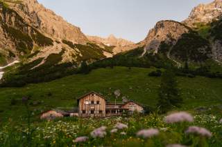 Hütte auf Wiese vor Talschluss, davor eine Blumenwiese.