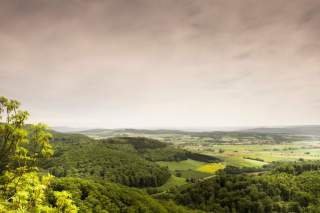 Blick über grüne, bewaldete Hügel und landwirtschaftliche Flächen unter bewölktem Himmel.