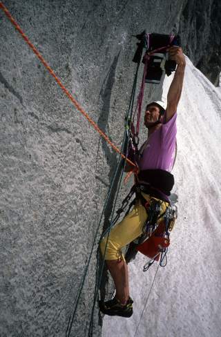 Ein Kletterer mit Helm und Kletterausrüstung klettert an einer steilen Felswand, gesichert mit mehreren Seilen.