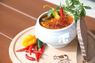Weiße Schüssel mit Chili con Carne, garniert mit Chilischoten und Petersilie, auf einem Holzbrett neben einer Scheibe Brot und verschiedenen frischen Chilischoten.