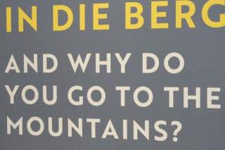 Text auf grauem Hintergrund mit gelben und weißen Buchstaben: „IN DIE BERG AND WHY DO YOU GO TO THE MOUNTAINS?“