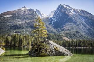 Fels in Bergsee mit Gipfeln im Hintergrund