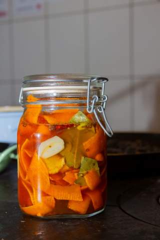 Ein Einmachglas mit eingelegten Karottenscheiben, Knoblauch und Gewürzblättern steht auf einer Küchenarbeitsplatte vor einem Fliesenspiegel.