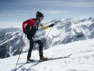 ein Skimo Athlet im Aufstieg. Im Hintergrund sind schneebedeckte Berge.