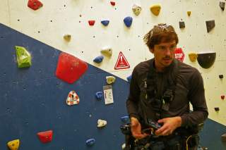 Routenbauer steht vor einer Kletterwand mit verschiedenen Griffen und Tritten.
