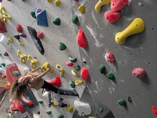 Kind klettert an einer bunt bestückten Boulderwand in einer Kletterhalle.