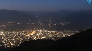 Blick auf die beleuchtete Stadt Innsbruck in der frühen Morgendämmerung mit Bergen im Hintergrund und klar erkennbarem Straßenverlauf.