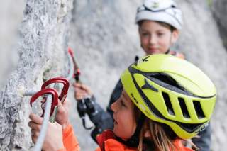 Zwei Kinder mit Kletterhelmen sichern sich an einer Felswand beim Klettern.