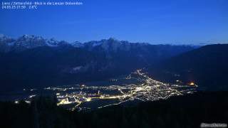 Erleuchtete Stadt in der Nacht, im Hintergrund steile Berge mit Schnee gezuckert.