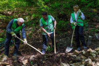 Drei Menschen schaufeln auf einem Alpinweg.