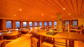 Innenraum eines runden, gemütlichen Restaurants mit Holzdecke, Holzbänken und Tischen, die eine Panorama-Aussicht auf die Berge bieten.