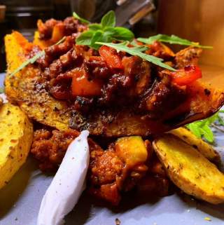 Gefüllter, gebackener Kürbis mit würziger Hackfleisch-Tomaten-Mischung, garniert mit frischen Kräutern, serviert mit Kartoffelwedges und einem Klecks Sauerrahm.