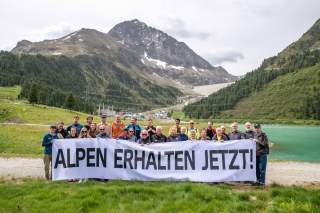 Die Vertreter*innen der Verbände stehen vor Bergen, im Hintergrund ist das Staudammprojekt im Längental zu sehen.
