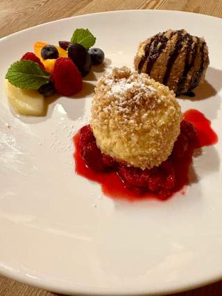 Dessertteller mit Topfenknödel, einem mit Puderzucker und Himbeersauce, der andere mit Schokoladensauce, dazu frische Beeren und Minzblätter.