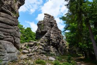 Felsformationen umgeben von grünem Wald unter einem blau-weiß bewölkten Himmel.