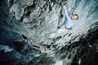 Kletterin mit Helm und Kletterausrüstung hängt an einer steilen Felswand in großer Höhe.