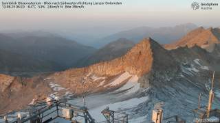 Blick vom Sonnblick Observatorium auf felsige Berggipfel und Gletscherreste in den Lienzer Dolomiten bei Sonnenaufgang. Im Vordergrund sind Wettermessinstrumente und -stationen zu sehen.