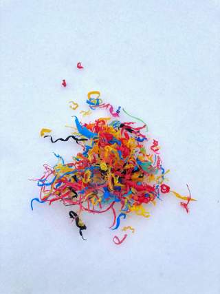 Bunte, zerkrümelte Plastikstreifen liegen als Haufen auf weißem Schnee.