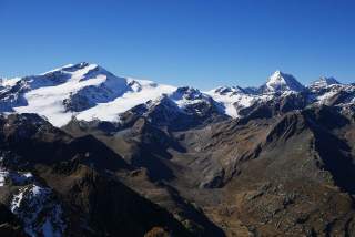 Berglandschaft mit schneebedeckten Gipfeln unter klarem blauem Himmel.