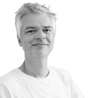 Porträt eines lächelnden Mannes mit kurzen, grauen Haaren, der ein weißes T-Shirt trägt, vor weißem Hintergrund.