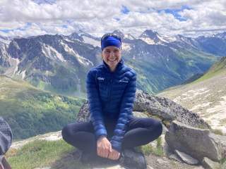 Johanna Felber sitzt im Schneidersitz vor einem Hochgebirgspanorama