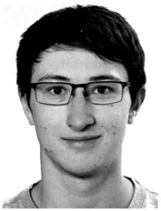 Porträt eines jungen Mannes mit kurzen dunklen Haaren und einer Brille, der in die Kamera blickt.