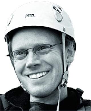 Porträt eines lächelnden Mannes mit Brille und Kletterhelm.