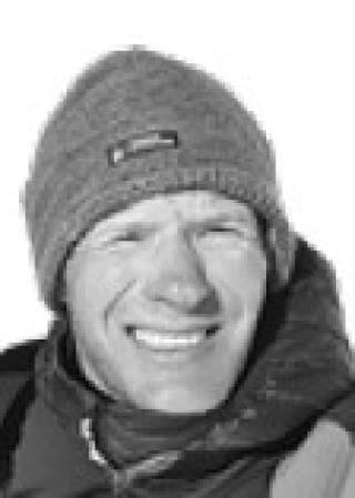 Porträt eines lächelnden Mannes mit Mütze und Outdoor-Jacke vor hellem Hintergrund.